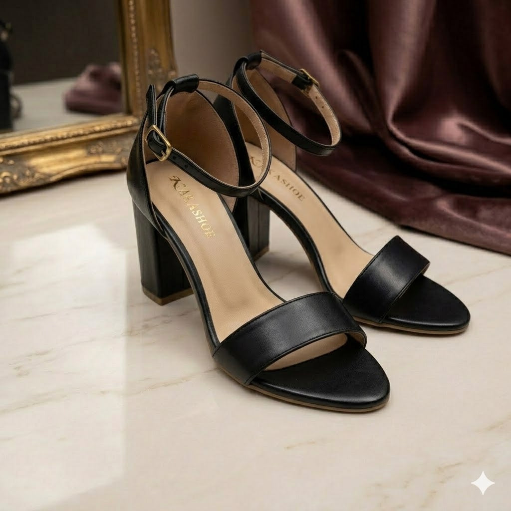 Black high-heeled sandals on a light surface with a mirror and fabric in the background